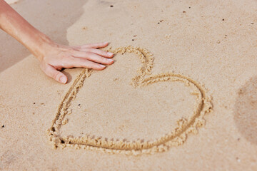 Hand drawing heart in sand on sandy beach with ocean in background