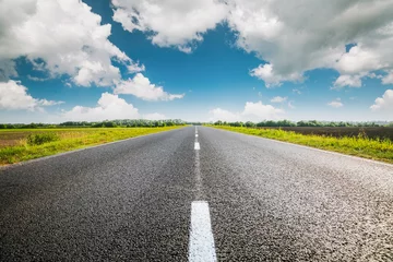 Fototapete Rund A straight asphalt road passing through agricultural fields under a blue sky with white fluffy clouds stretching into the distance. © Leonid Tit