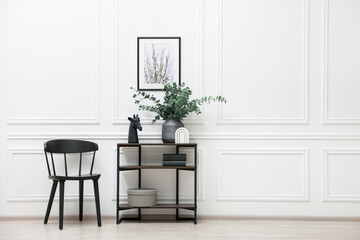 Console table with decor and chair near white wall in room, space for text. Interior design