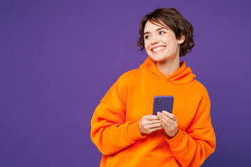 Young smiling happy Caucasian woman she wear orange hoody casual clothes hold in hand use mobile...