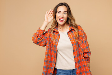 Young curious nosy smiling woman she wears orange shirt casual clothes try to hear you overhear listening intently isolated on plain pastel light beige background studio portrait. Lifestyle concept.