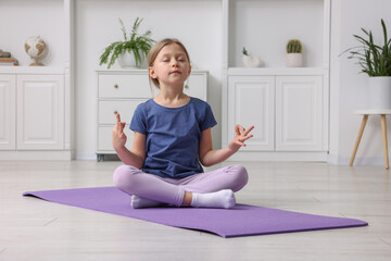 Cute little girl exercising on fitness mat indoors