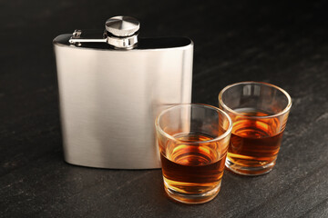Hip flask and shot glasses of whiskey on black table, closeup