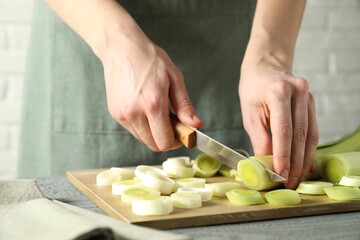 Woman cutting fresh leek at grey wooden table, closeup