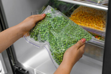 Woman taking plastic bag with frozen green peas from refrigerator, closeup