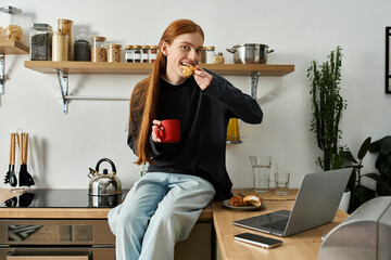 A young redhead man relaxes at home with coffee and snacks while using his laptop.