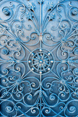 A view of an intricately designed metal gate with floral and geometric patterns. The artistic...