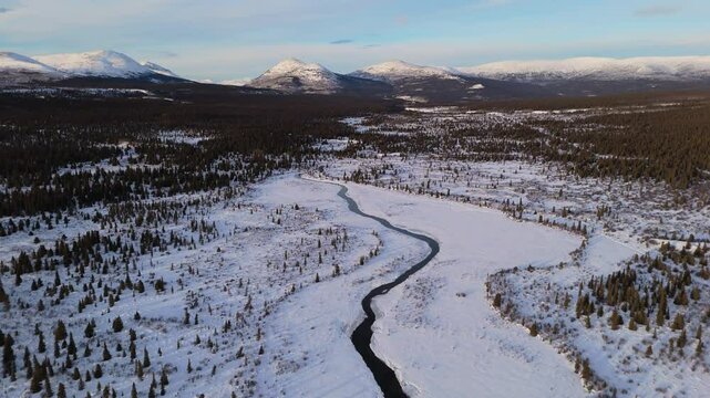 Panoramic aerial tilt up over Yukon River near Fish Lake in Whitehorse. The snow-covered Canadian wilderness and Northern Territory gleam under sub-zero winter skies.