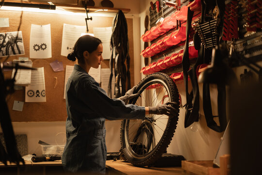 Hobby Diy and leisure concept. Young brunette woman repairing bicycle wheel while standing in bicycle workshop or home garage