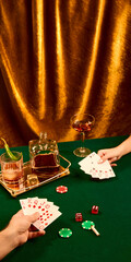 Still life photography, Man and woman playing cards, sitting at table with whiskey glasses, poker chips and dice against golden curtain. Luxury and drama. Concept of party, celebration, high-society