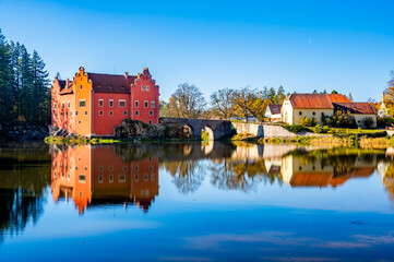 Obraz premium Panoramic view of Cervena Lhota Castle in the Czech Republic, surrounded by a lake reflecting its image. Autumn trees in vibrant colors and sunny weather create a picturesque, serene scene.