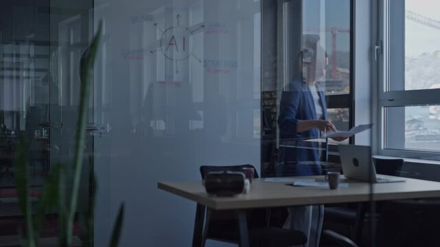 Young businesswoman in a modern office reviews documents in natural light, with a glass board featuring an AI concept diagram in the background. Concept of technology and innovation in a workspace