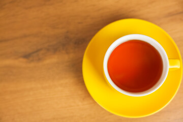 A yellow cup with a saucer in which black tea is poured stands on a wooden background, a top view with space for text. The concept of tea drinking, tea traditions. High quality photo