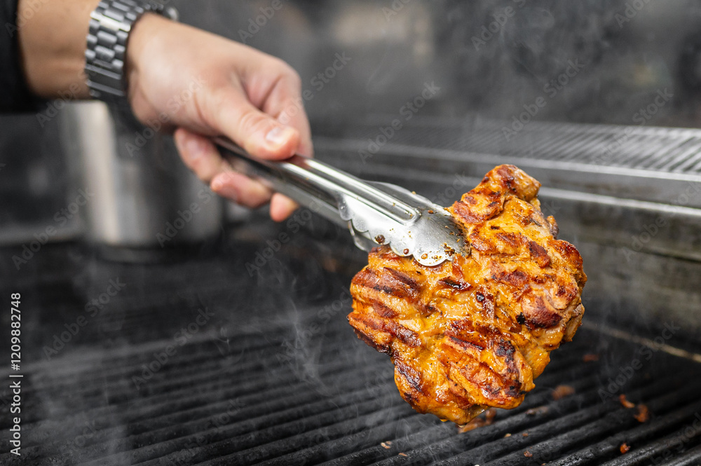 Canvas Prints A close-up of a hand holding tongs, flipping a large, juicy piece of grilled meat on a smoky barbecue grill. The image captures the essence of outdoor cooking and delicious food preparation.