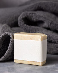 Beige handmade soap bar with blank label near dark grey folded towel closeup, mockup