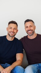 Fototapeta premium Two men are sitting on a couch, smiling and looking at the camera. Scene is happy and friendly