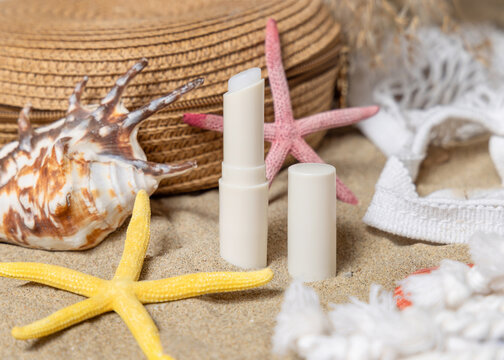 Opened sunscreen lip balm stick near starfishes and seashells on a sandy beach, cosmetic mockup