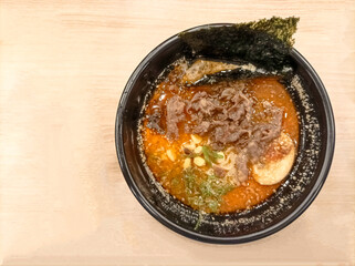 Japanese cuisine. Ramen noodle soup with sliced beef, egg, chives, sprouts and a piece of seaweed in a black bowl on an isolated wooden table.
