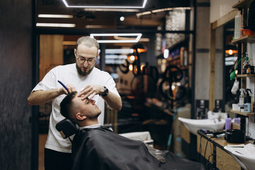 Obraz premium a photo of a professional barber focusing on the work of a client in a barber chair in front of a mirror in a modern barbershop