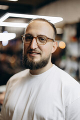 smiling portrait of a man with a goatee and glasses wearing a white T-shirt with a blurred evening...