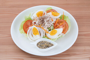 Chicken breast salad, boiled eggs and Japanese sesame dressing in a white ceramic plate. On a pine wood tabletop. Healthy food concepts with calorie control.