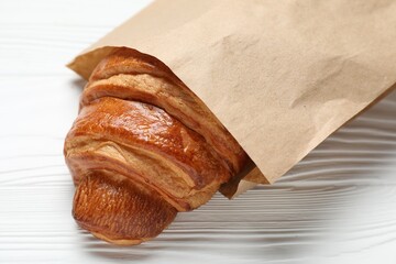 Paper bag with fresh croissant on white wooden table, closeup