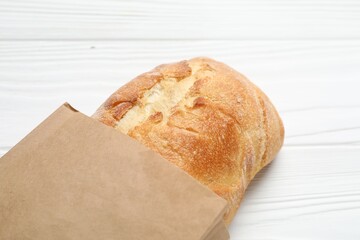 Paper bag with fresh baguette on white wooden table, closeup
