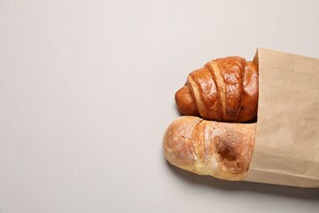 Paper bag with fresh baguette and croissant on light gray table, top view. Space for text