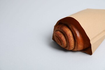 Paper bag with freshly baked bun on white background, closeup. Space for text