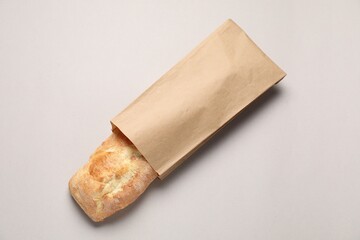 Paper bag with fresh baguette on light gray table, top view