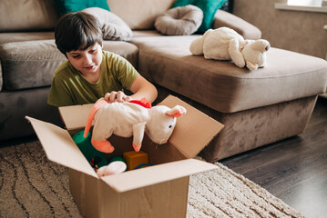 Happy cheerful kid boy packing his toys for delivery donation box. Charity and recycling