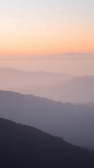 Fototapeta premium Dreamy Pastel Sunset Over Misty Mountain Layers: A Soft and Tranquil Landscape Capturing Subtle Gradients of Pink, Peach, and Blue Hues in an Ethereal Atmosphere for Phone Wallpaper
