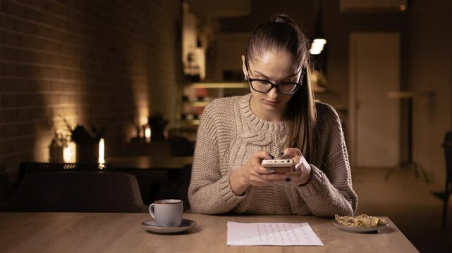 Woman working remotely in the evening in a cafe scanning or photographing a receipt while making a payment using a mobile phone