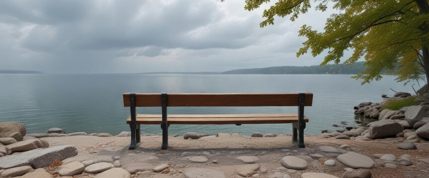 A quiet wooden bench sits atop the rocky shoreline of Pewaukee Lake gazing out onto the serene waters on a cloudy gray day, gray, outdoor, wisconsin