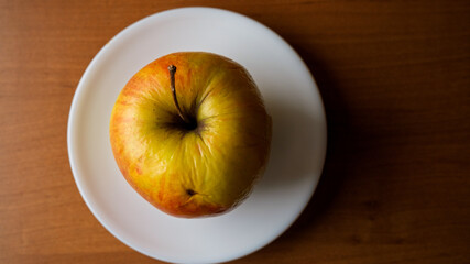 Bright yellow apple resting on a white plate against wooden background