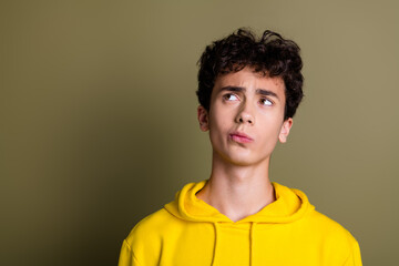 Thoughtful teenage boy in bright yellow hoodie posing against stylish khaki background © deagreez