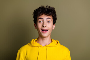 Joyful male teenager in a yellow hoodie against a khaki background expressing excitement