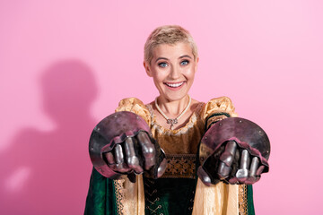 Smiling woman dressed in elegant medieval attire poses with knight gloves on a pink background
