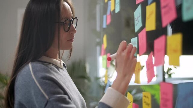 Asian Business Woman Write Tasks Creative Ideas On Sticky Notes On Glass Board, Female Corporate Leader Planning Project On Post It Sticky Notes Organize Work On Stickers