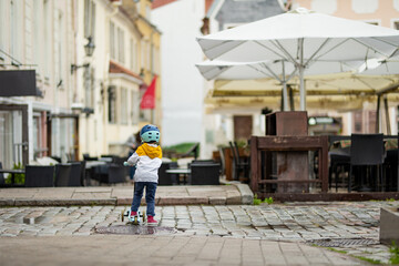 Cute little boy riding his baby scooter along colorful medieval streets of Tallinn Old Town or Tallinna Valalinn, included in the UNESCO World Heritage List. Child exploring Estonian capital