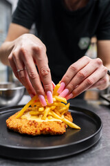 A close-up of hands expertly assembling a gourmet dish, featuring crispy fried chicken topped with golden French fries. The vibrant colors and textures create an enticing culinary scene.