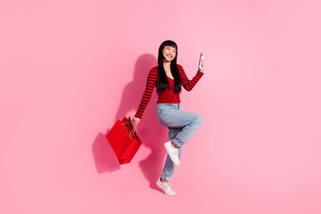 Young stylish woman smiling with shopping bags and phone in hand on a pink background