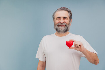 Smiling senior man holding small red heart promoting heart health and wellness