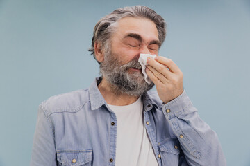 Senior man blowing his nose with closed eyes suffering from rhinitis