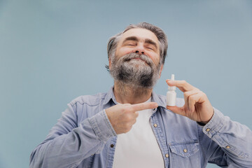 Senior man holding nasal spray and pointing at it with index finger