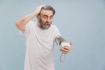 Shocked senior man checking blood pressure with electronic tonometer