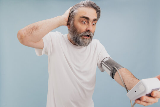 Shocked senior man checking blood pressure with digital monitor, suffering hypertension