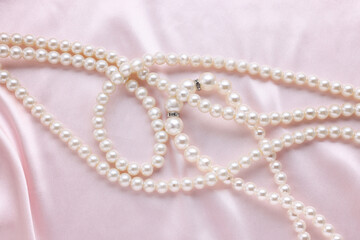 Elegant pearl necklace on pink fabric, top view