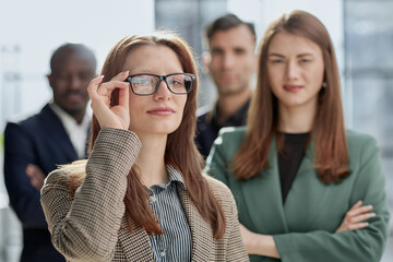 Obraz premium businesswoman in formal wear adjusting her glasses looking at the camera while standing in the office instead of with colleagues