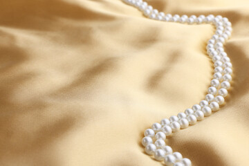 Beautiful pearl necklace on golden silk, closeup. Space for text